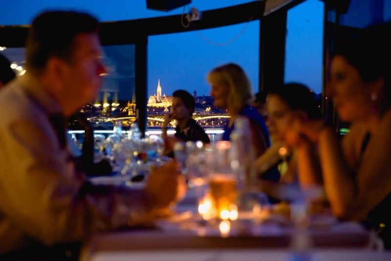 Guests on the panoramic terrace with the lit Buda side behind them